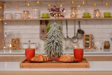 Fresh croissants on a plate, cups, Christmas tree on the background of Christmas kitchen.