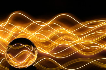 Long exposure photograph of neon gold colour in an abstract swirl, parallel lines pattern against a black background with reflections in a glass crystal ball. Light painting photography.