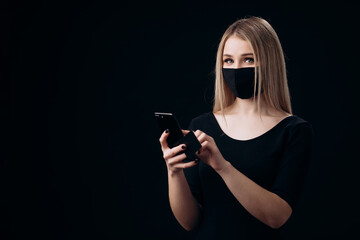 Cheerful woman in medical mask enjoying online shopping during quarantine. Happy lady using credit card and modern smartphone. Isolated over black background.