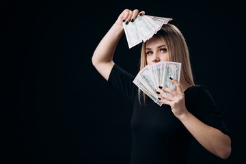 Stunning rich woman standing over black background with fan of money cash. Happy blonde posing in studio with dollars.