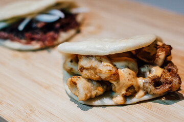 Fusion food bao with spanish fried squid and kimchi mayo and duck bao in the background on a bamboo table