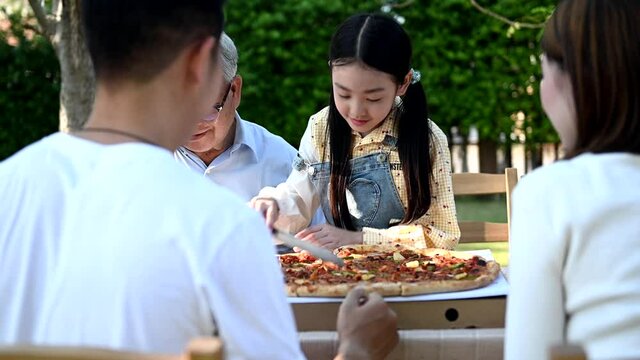 Asian family having pizza in garden at home. Parent with kid and grandfather lifestyle in backyard.