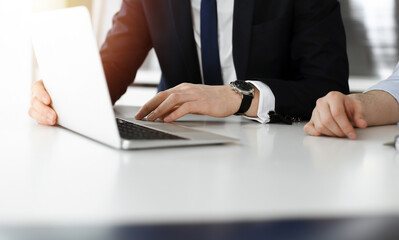 Fototapeta premium Unknown business people using laptop computer at the desk in modern office. Businessman or male entrepreneur is working with his colleague. Teamwork and partnership concept