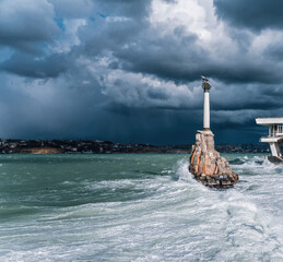 Monument to the flooded ships on the city embankment against the backdrop of the big wave in stormy...