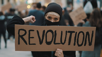 Young woman with face mask and banner protesing in the crowd. Revoultion concept. . High quality...