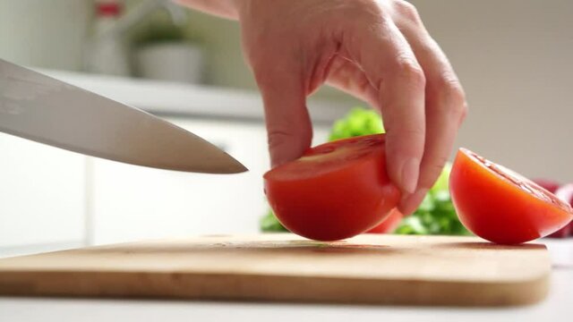 Close-up of female hands cut red tomato into slices with a knife.