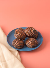 Traditional Russian vanilla marshmallow in chocolate glaze in a blue plate on pink background. Colorful table and linen textiles