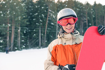 Portrait of a woman snowboarder wearing helmet and goggles in front of forest and slope