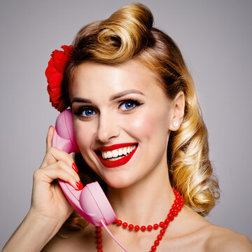 Face portrait photo - happy smiling woman holding telephone tube, saying allo. Pin up attractive girl. Blond model at retro and vintage studio concept. Grey background. Square.