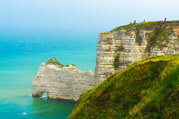 Fototapeta na wymiar Natural arch. Picturesque landscape of Etretat, Normandy, France. View from top, from the cliff down to the sea. Tops of chalk cliffs covered with green grass