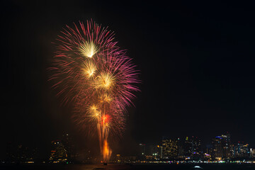 Fototapeta premium Firework festival with beach foreground and city background at Pattaya beach, Thailand. Colorful firework in celebration festival background
