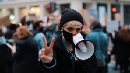 Woman with face mask and megaphone supporting anti-racism protests. Peace gesture. High quality...