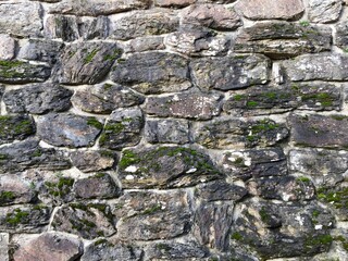 Old wall of wild stone overgrown with moss.