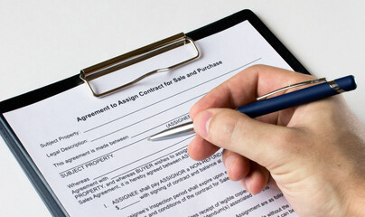 A man's hand with a pen signs a contract in a folder