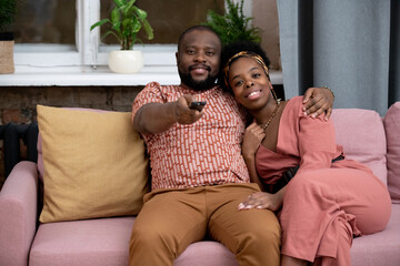 Happy young affectionate African husband and wife sitting on couch by window