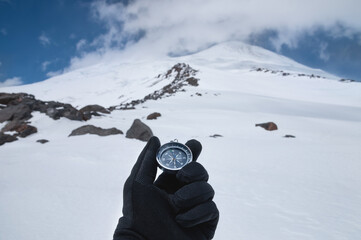 A man's hand in a black glove holds a magnetic compass against the background of a snow-covered...
