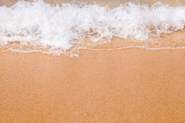 Foam of the ocean surf wave covering wet beach sand with sun glowing.