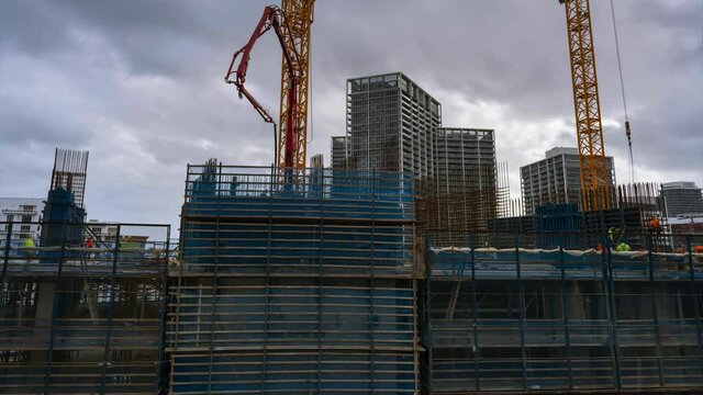 Construction of skyscraper slip forming core pillars with workers setting ribs helped by crane and pouring cement from pump aerial time lapse 