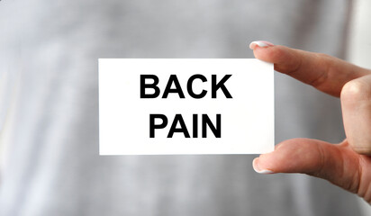 The girl holds a business card in front of her with the text BACK PAIN. You can only see your hands.