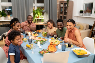 Happy African family talking to their friends in video chat by festive table