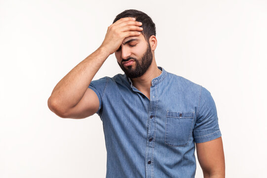 Upset frustrated man holding forehead with hand, making facepalm gesture, lost all his money, forget about date, big failure. Indoor studio shot isolated on white background