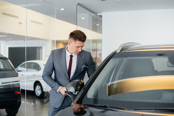 A young businessman looks at a new car in a car dealership. Buying a car