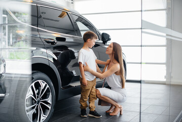 A happy mother with her young son chooses a new car at a car dealership. Buying a car