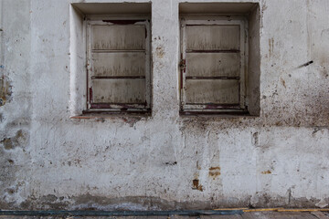 Front side interior view of old rough dirty white scratch concrete wall with two rectangular windows inside abandon industrial building.