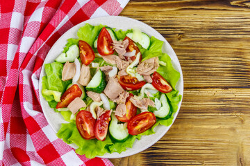 Tasty tuna salad with lettuce and fresh vegetables on wooden table. Top view