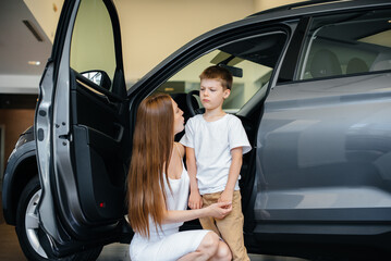 A happy mother with her young son chooses a new car at a car dealership. Buying a car