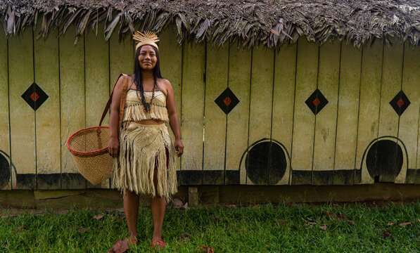 Indigenous woman from the Huitoto tribe of the Colombian Amazon in front of a maloka with a traditional basket