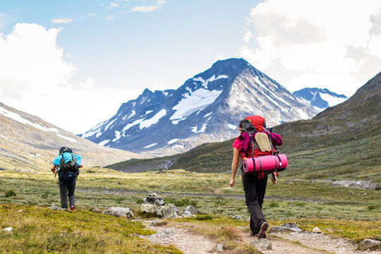Rear view shot of two female hikers going through grass trail with awesome view to snowy mountains in Norway
