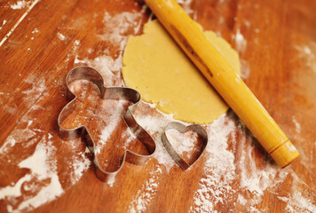 forms for baking gingerbread in the shape of a man and a heart on the background of a rolling pin and rolled dough close-up