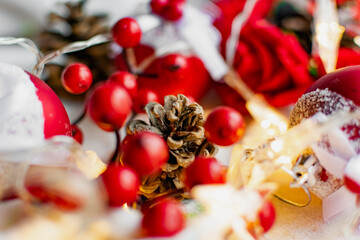 Christmas decorations on a soft cozy white blanket. Red toys in the form of balls and berries, with fir cones. Around yellow lanterns light bulbs in the form of stars. Elegant composition for Christma