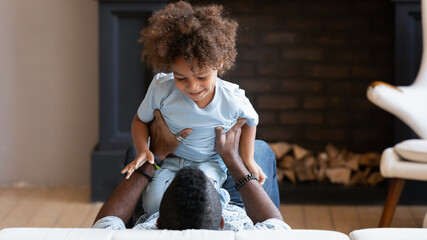 Ticklish. Lovely small african preschool boy playing funny game on sofa in bedroom with beloved...