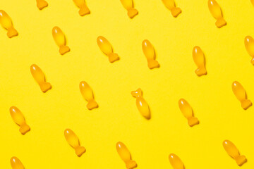 Seamless pattern with fish-shaped cod liver oil capsules on bright yellow background. Healthy lifestyle concept. Omega 3 fish oil capsules with vitamin D for children.