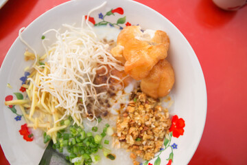 Pork rice porridge with soft-boiled egg, deep-fried dough stick, sliced ginger, spring onion and fried garlic served with hot chinese tea at local morning market.