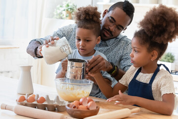 Cooking with daddy. Caring concentrated african foster father teaching two focused interested...