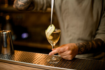 view of bartender decorates cocktail glass with cucumber slice using tweezers