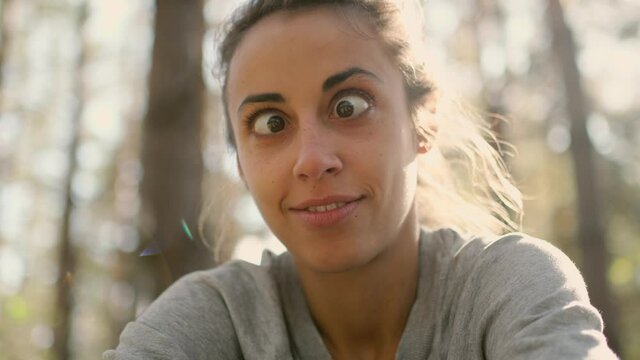 close up happy young woman laughs and grimaces looking straight at camera. POV, girl spending time with some one in woods getting fun