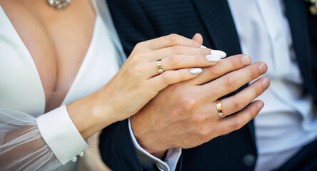 Hands of the bride and groom close-up, blurred background. Gold wedding rings on the fingers of newlyweds. Concept of marriage.