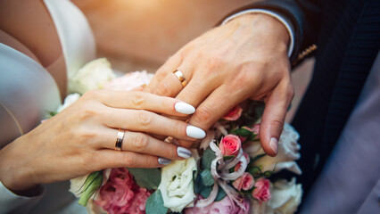 Obraz na płótnie Canvas Hands of the bride and groom on the background of wedding bouquet, top view, blurred background. Gold rings on the fingers of newlyweds, close-up.