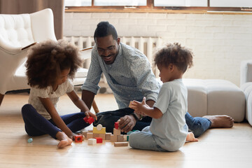 Father on vacation. Interested black dad engaged in building wooden brick towers with school age...