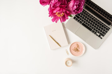 Home office desk workspace with laptop, pink peony flowers bouquet and notebook on white background. Flat lay, top view freelance work concept.