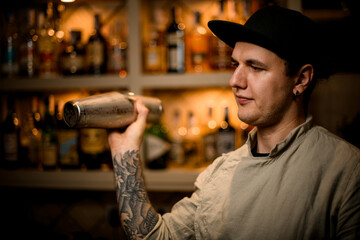 young guy holds steel shaker in his hand and mixes cocktail in it