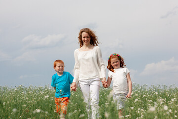 Redhead kids having fun with mom in green grass on background of blue sky