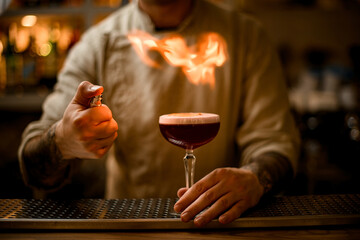 bartender make fire over glass with foam cocktail on bar counter
