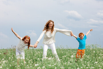 Fototapeta premium Redhead kids having fun with mom in green grass on background of blue sky