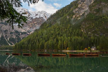 A view of the lake Pragser Wildsee in the Dolomites with a chain of boats, mountains and woods in autumn in South Tyrol, Italy.