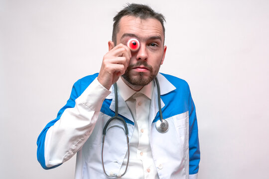 Evil doctor holds colored eyeballs near his face. Concept of a creepy doctor